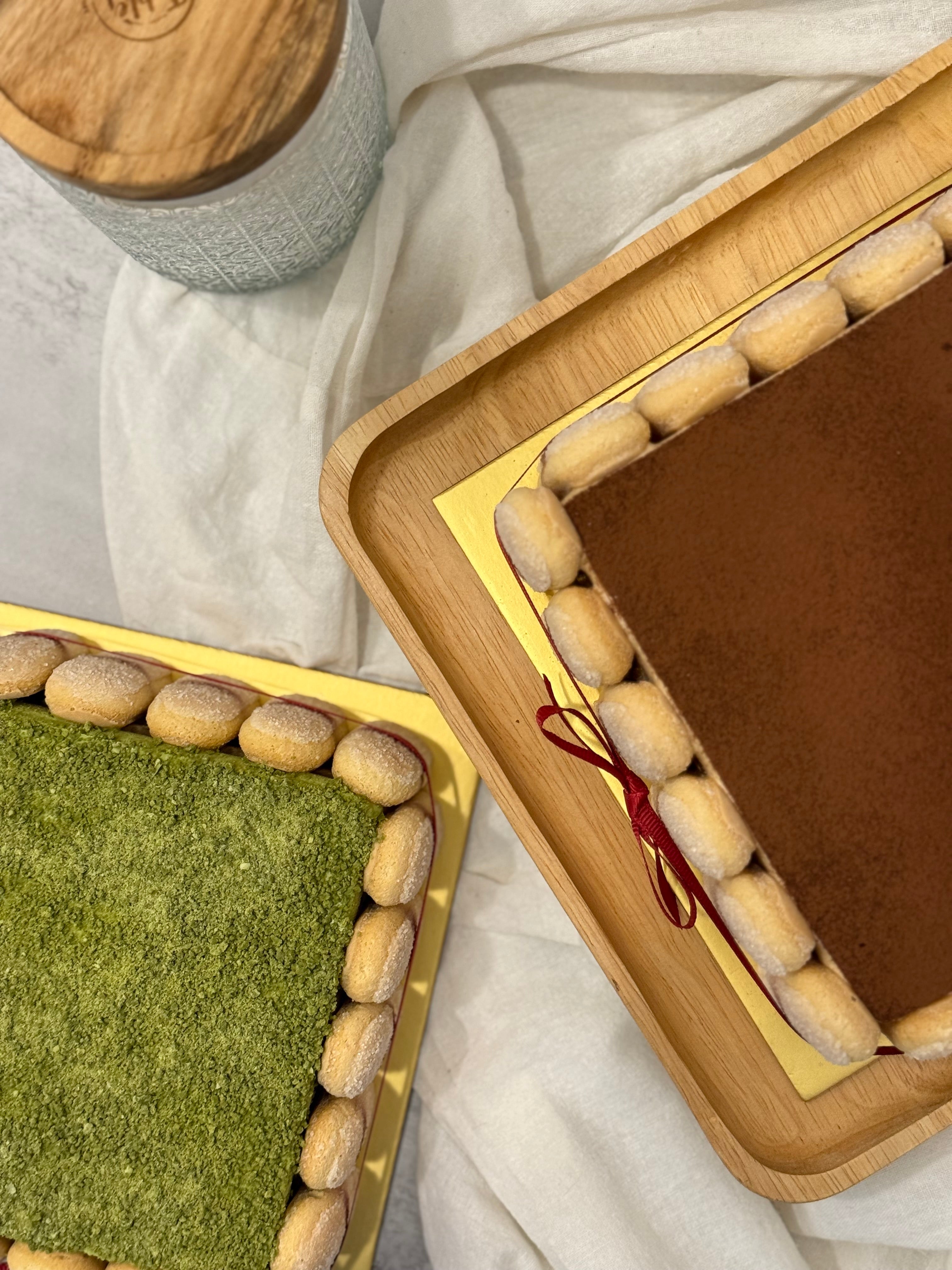 Two square tiramisus in wooden trays with a red string on a light fabric background