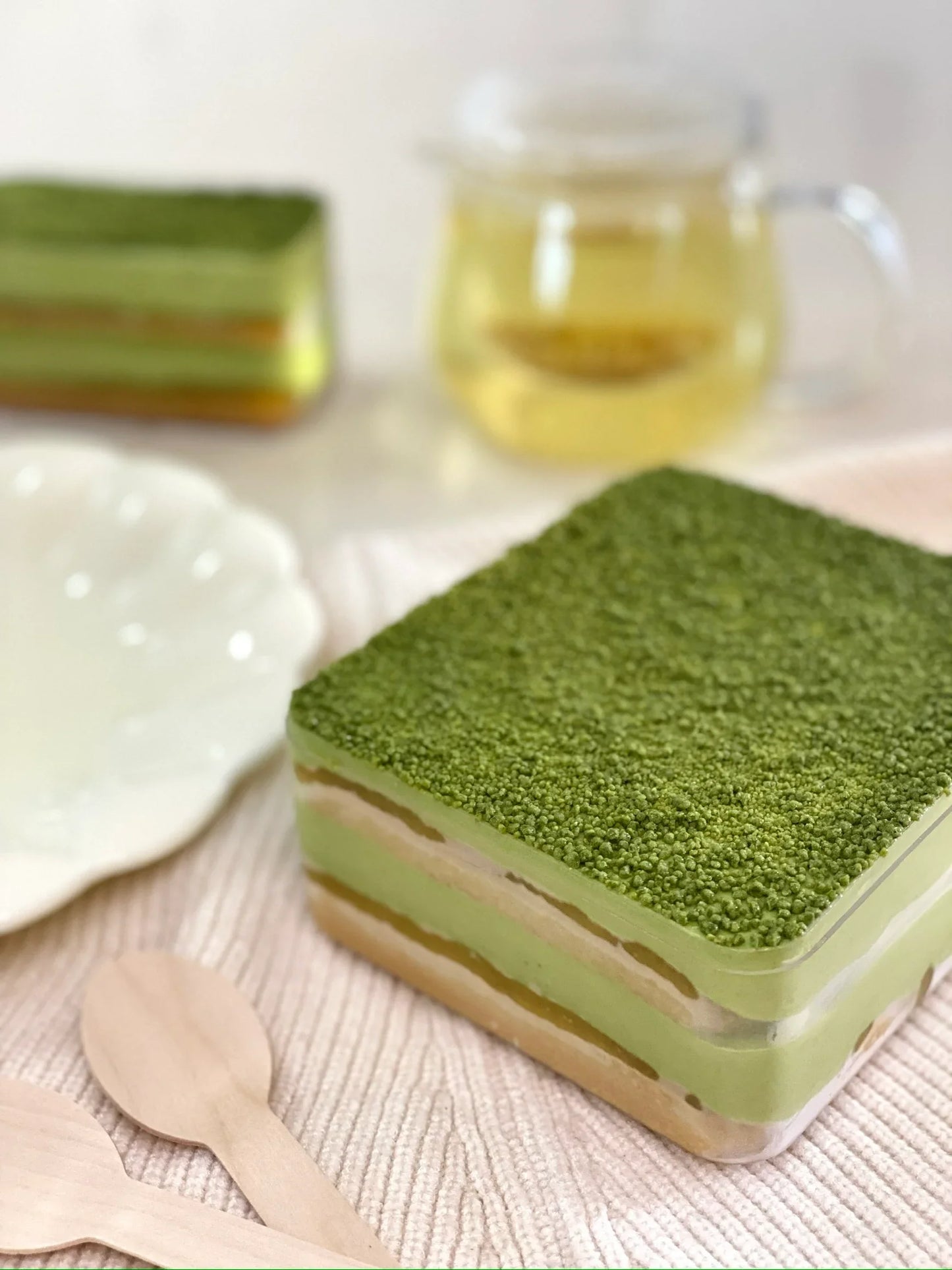 Green layered tiramisu dessert on a white surface with a cup of tea in the background