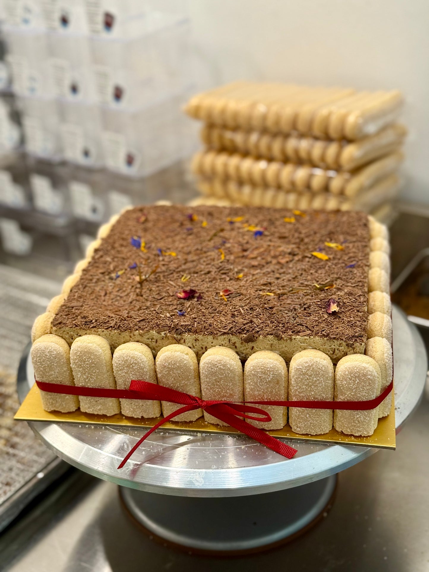 Square tiramisu cake with a red ribbon on a metal stand