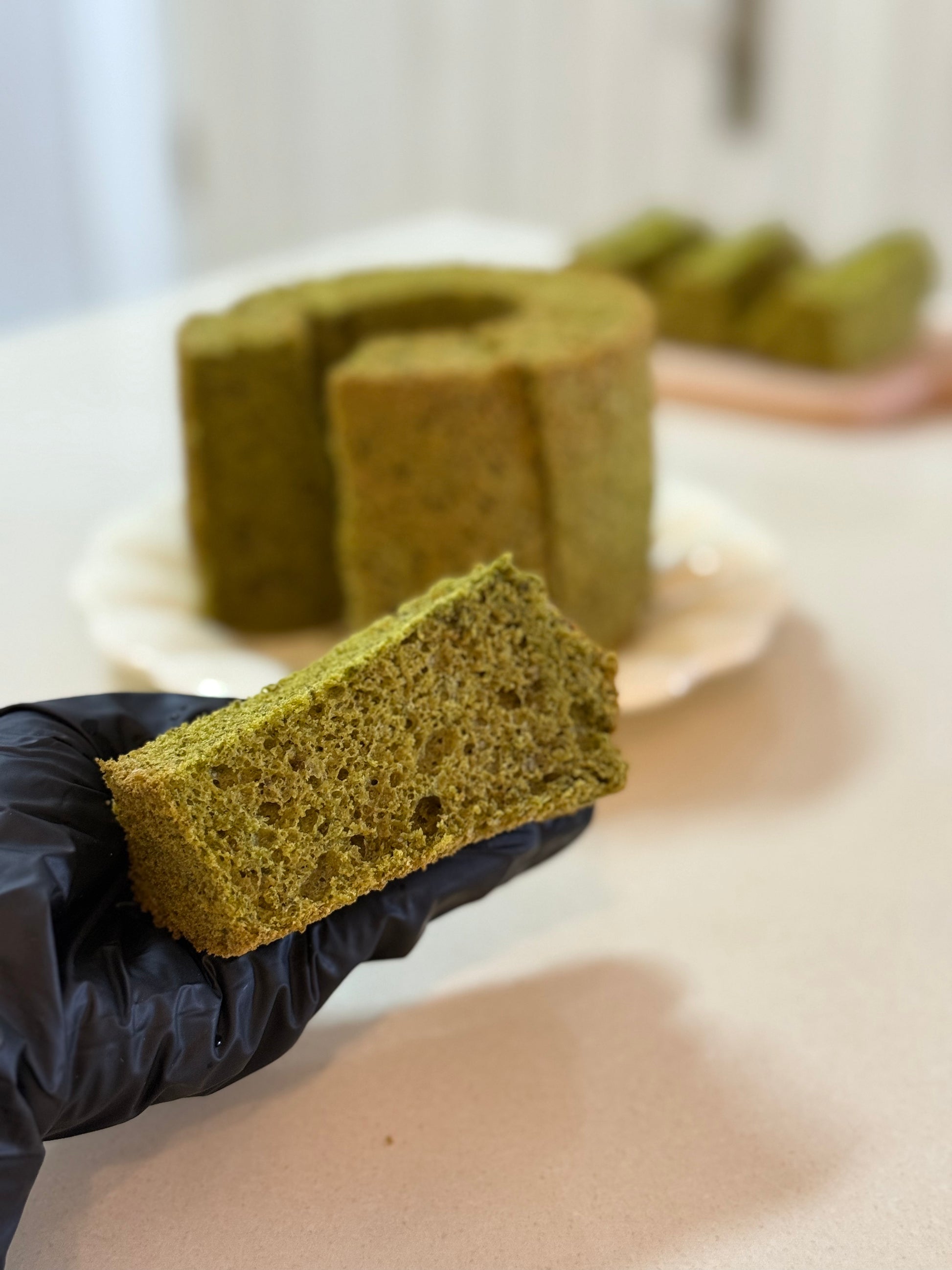 A slice of Matcha Chiffon Cake with the whole Chiffon cake in the background. Uniquely Singapore