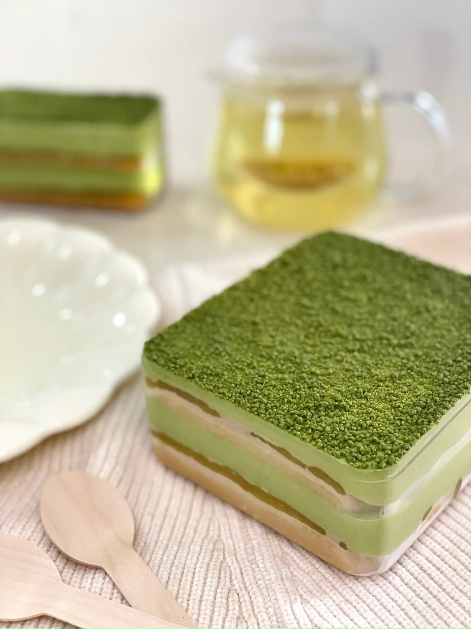 Green layered tiramisu dessert on a white surface with a cup of tea in the background