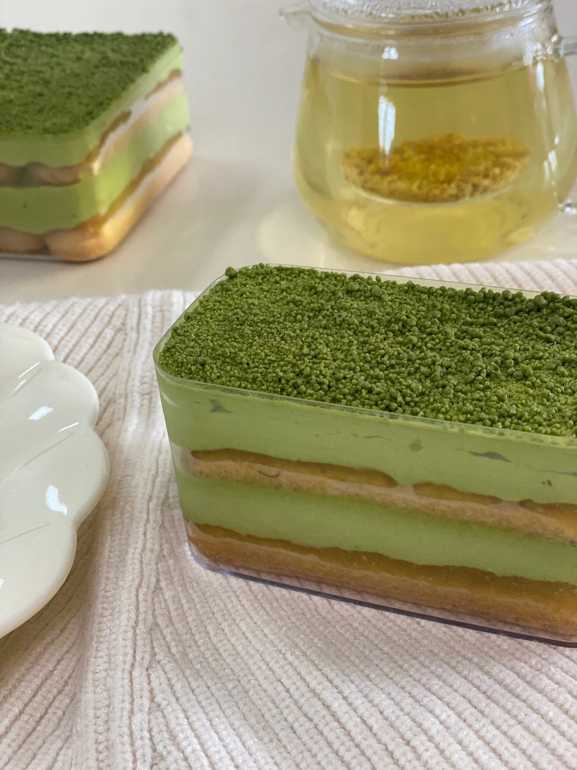 Green tea tiramisu in a tub with matcha powder on a textured surface