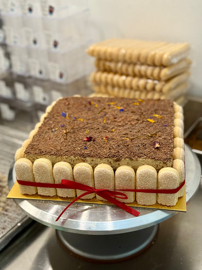 Square tiramisu cake with a red ribbon on a metal stand