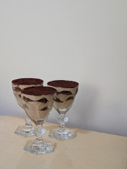 Three glass dishes with a Tiramisu layered dessert on a beige surface and light gray background